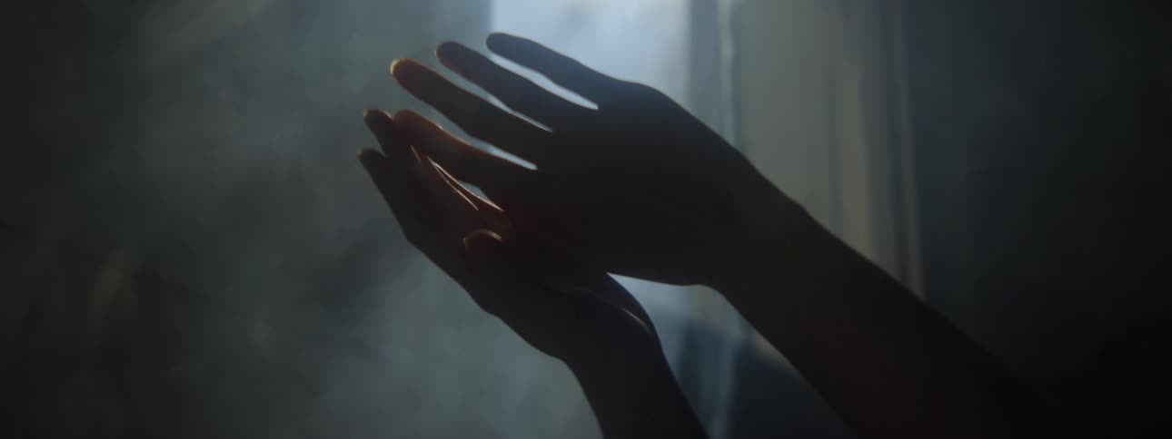 A females hands are held aloft in a room that is filled with steam