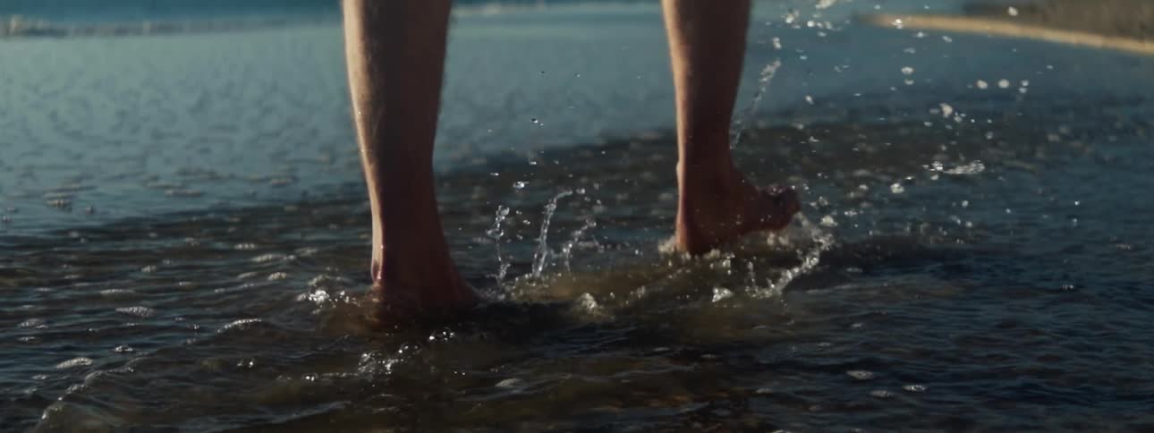 Man in barefeet walks along the beach splashing water