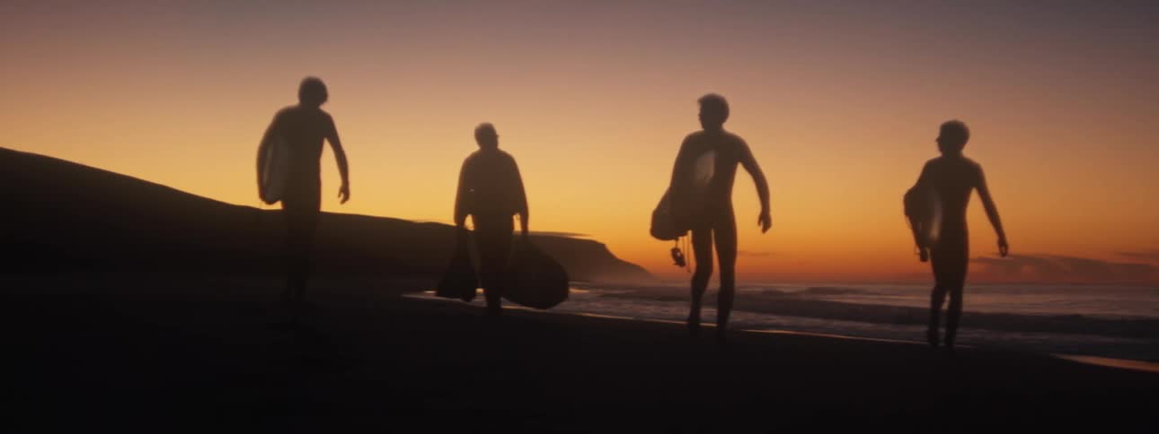 The silhouette of surfers walking on the sand carrying their boards at sunrise