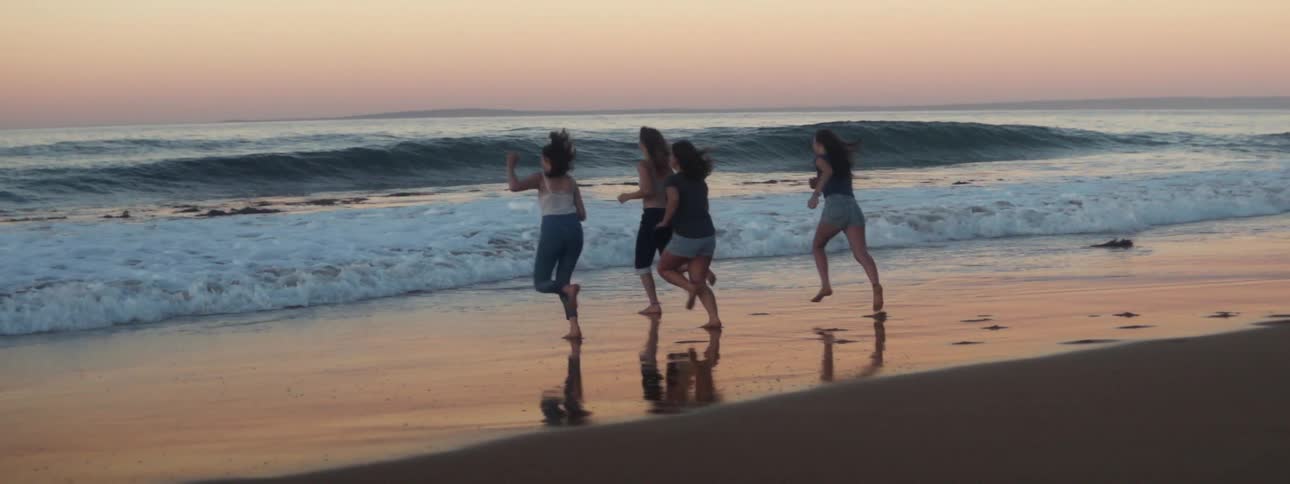 A group of girls runs to wavy ocean on the beach at sunset