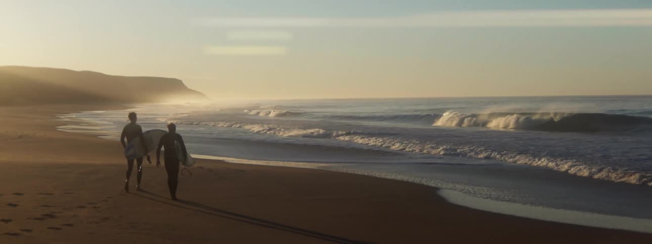 Two surfers walk on the coast