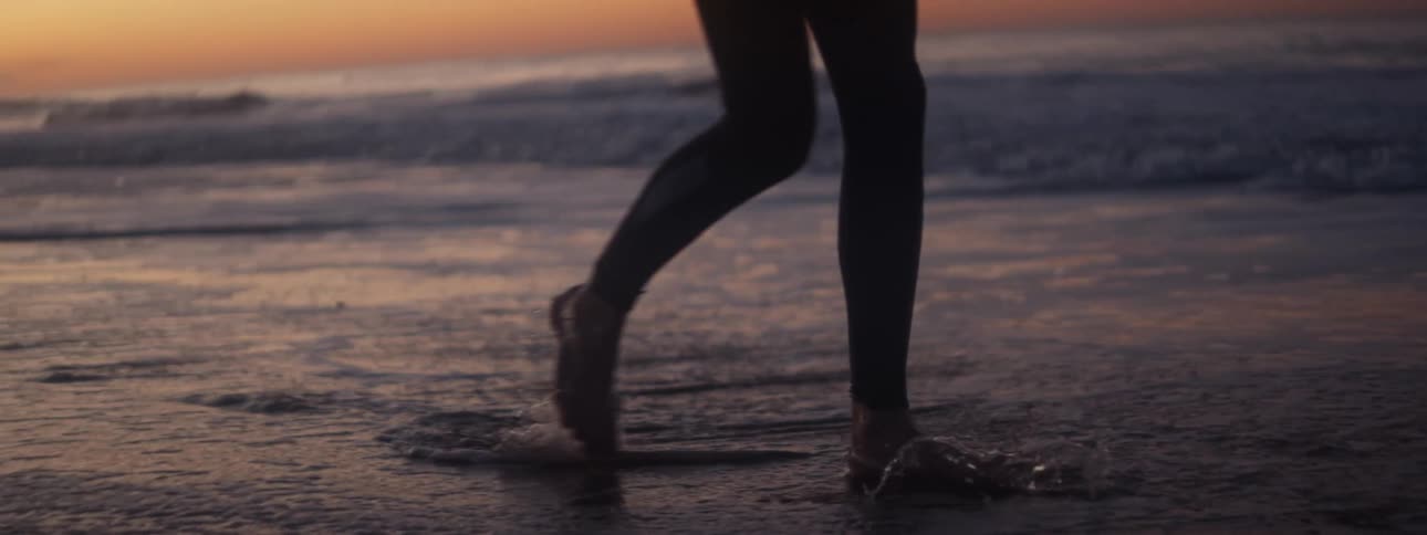 Woman wearing yoga pants walks barefoot on the beach at sunset next to the sea