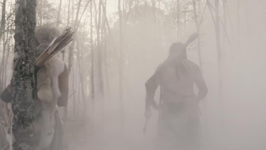 Men carrying weapons walk into a smoke filled forest