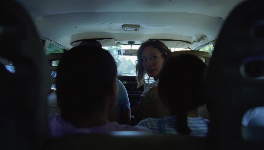 Mother sitting on the passenger seat of a car turns around to yell at their daughters