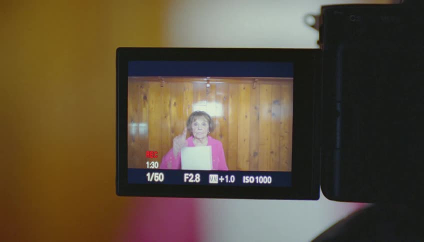 A woman stands in front of a camera and starts to read from a piece of paper