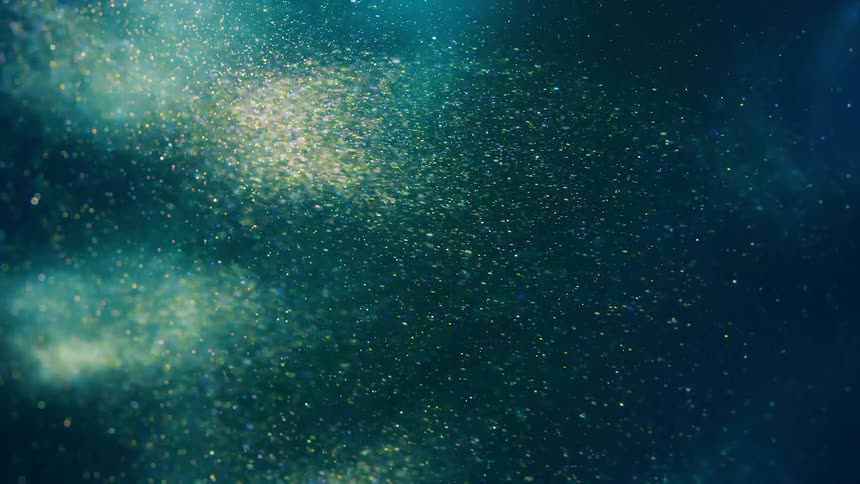 Light illuminates a cloud of glittering particles as they pass before an aqua backdrop