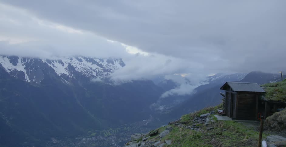 A small shed on a ledge high in the mountains on a cloudy day