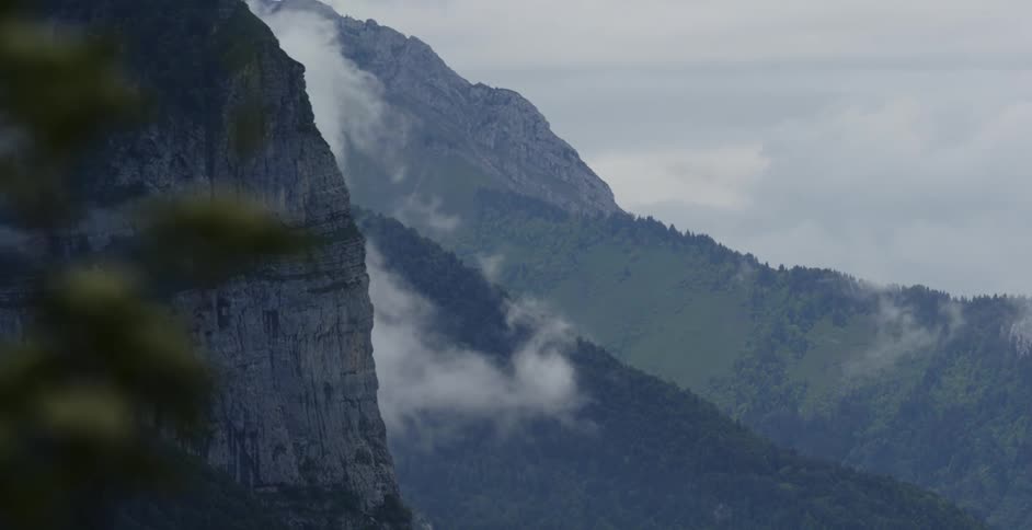 A mountain slope covered in forest and clouds during the day