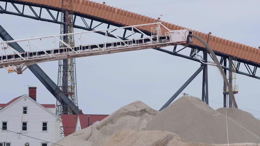 A crane is used to add more sand to a tall pile of sand at a construction site