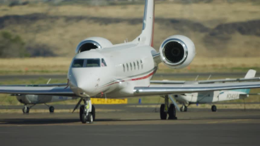 A private jet is parked on the ramp as seen from an arriving vehicle or airplane at the airport