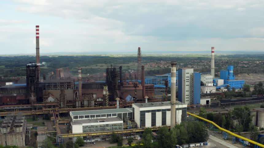A steel factory with pipelines and smokestacks under a cloudy sky in Eastern Europe