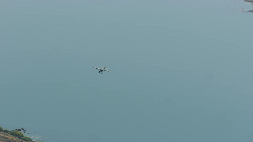 A small Carbon Cub FX3 plane flies over a waterway in the countryside during the day