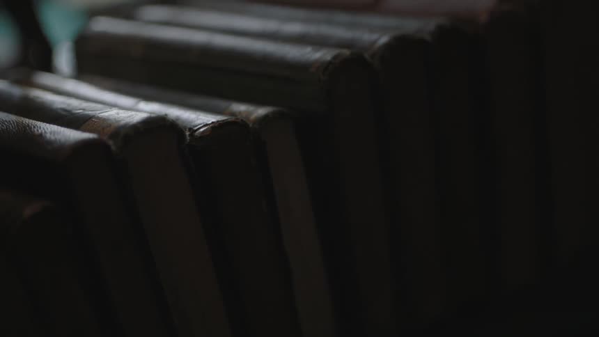 Old leather-bound books stacked in a row in a dark room