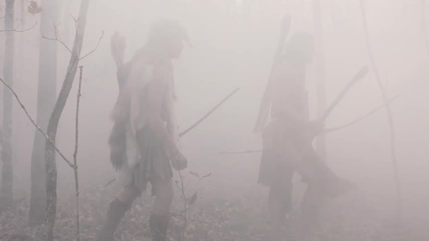 Several native american people with bows walk among the trees