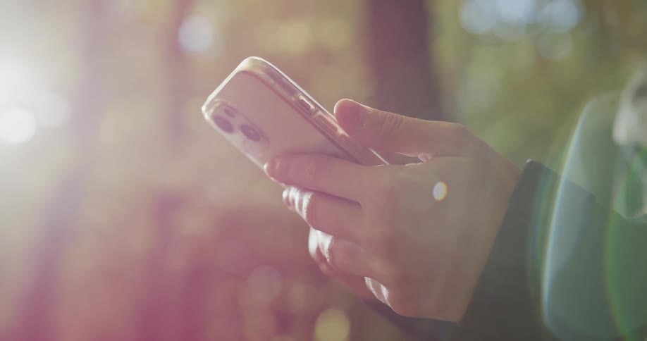 The sun shines brightly upon a woman holding a cell phone in her hands