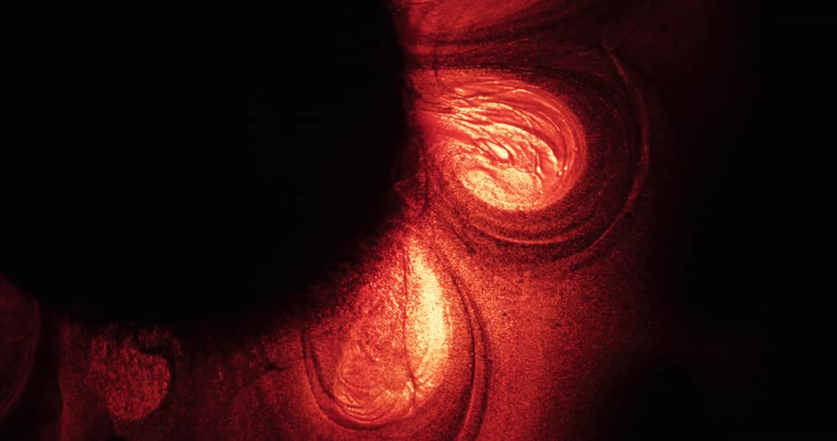 Glowing red and orange particles are moving and swirling in the darkness