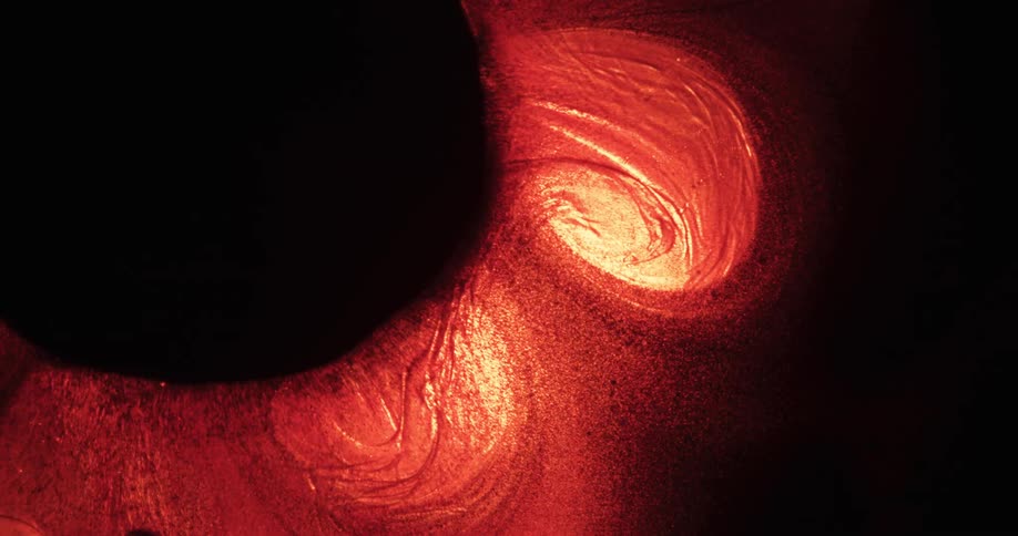 A red and yellow glowing substance ripples and slowly swirls in the darkness as particles of dark matter move to the organic black mass