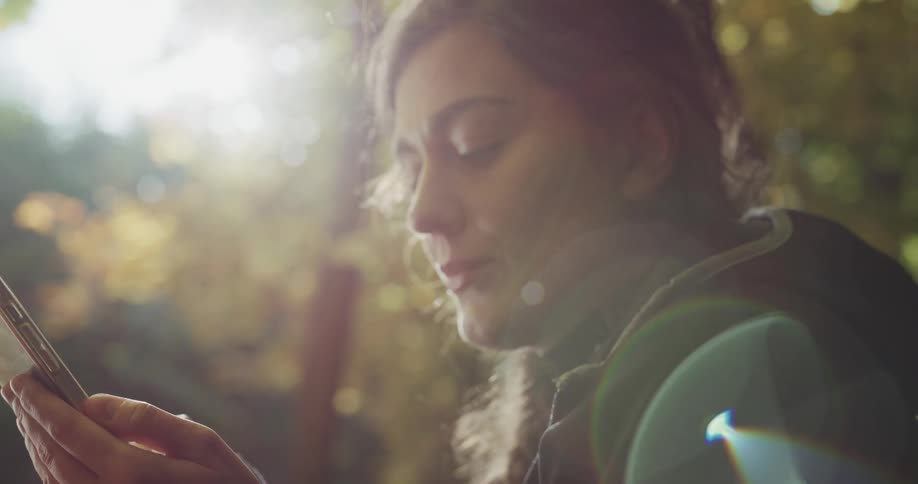 A teenage girl sits outside and texts on her cell phone