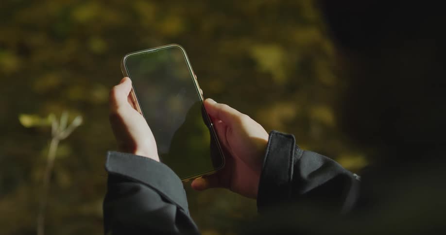 A person is standing outdoors and holding a cell phone