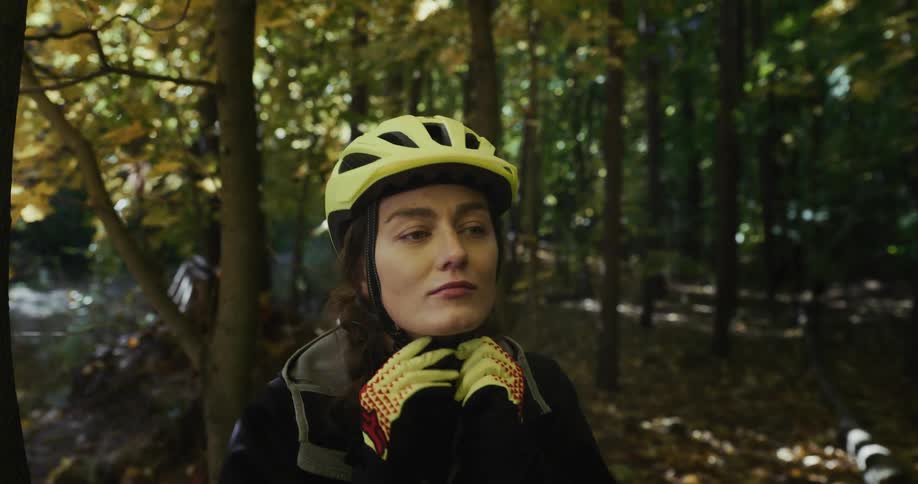 A woman puts on a bicycle helmet and walks toward a trail in the woods