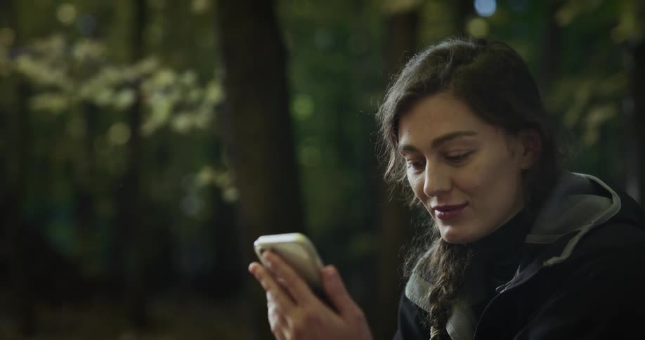 Woman smiles while scrolling on smartphone in woods