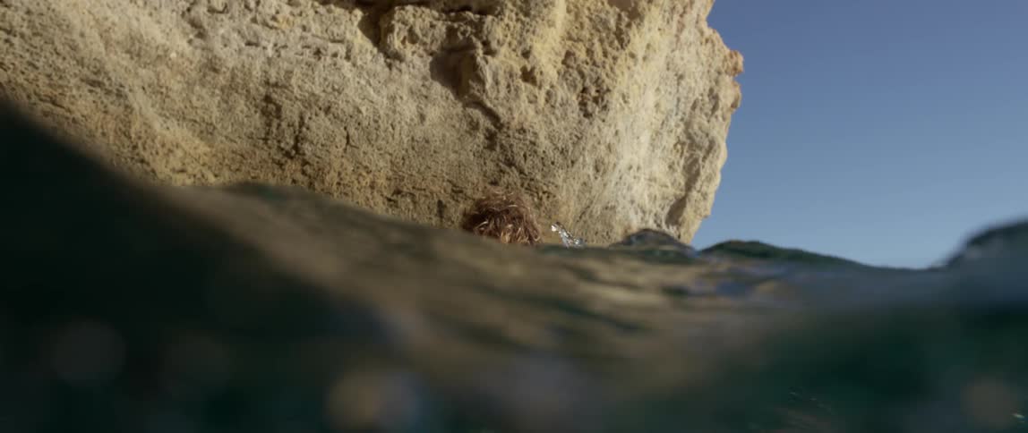 Man wearing wetsuit floats on surfboard near large rock
