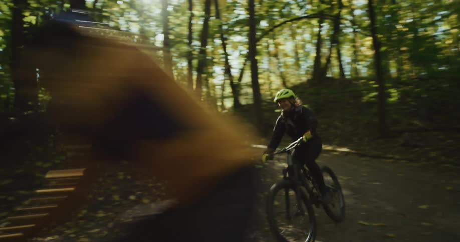 The sun shines brightly through the trees as two people ride their bicycles on a path through the woods