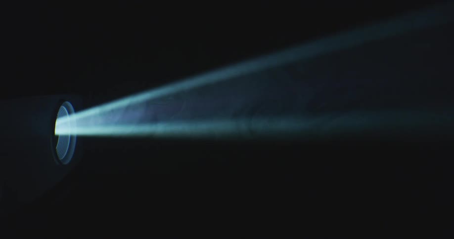 A ray of light emits from a projector as smoke moves inside the light in the darkness