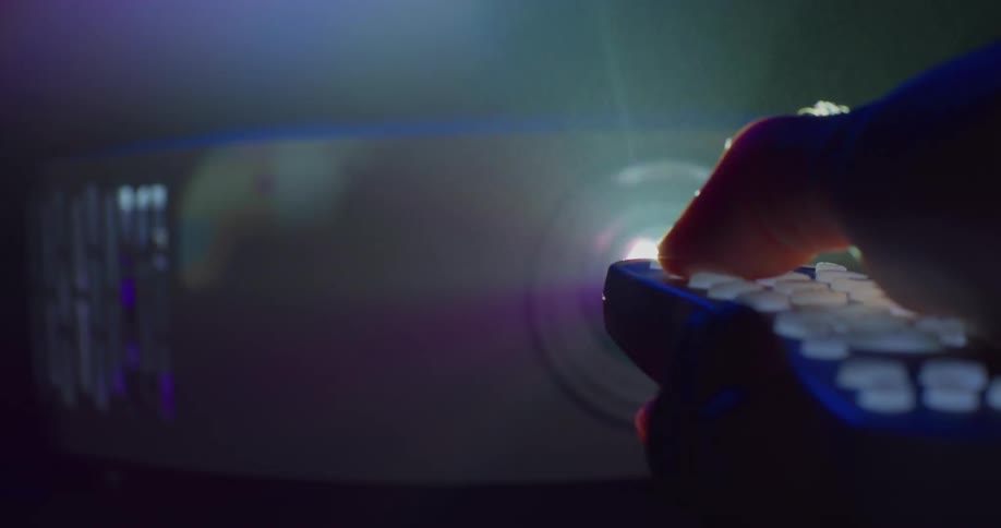 Light is shining brightly from a projector and someone holds a remote control in front of the light