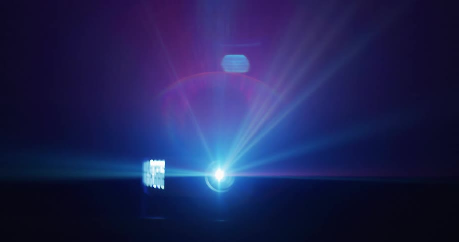 A projector is on a table in the darkness emitting moving blue rays of light