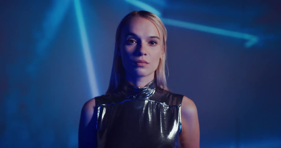 A woman looks up and at the camera as lines of light move around behind her