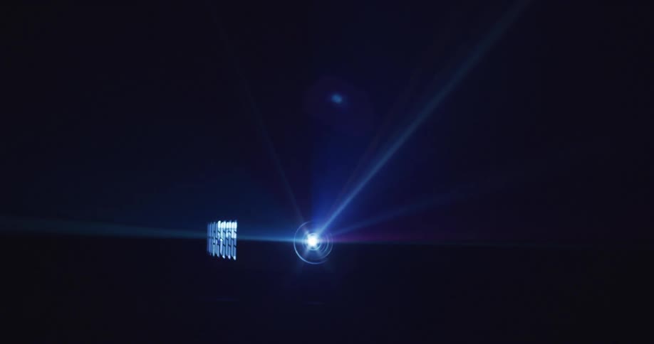 A projector emits a bright purple light in a large dark room