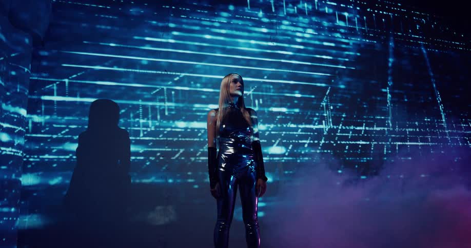 A woman with long blond hair wearing a black latex outfit is standing in a room with magenta colored smoke and light blue lines of light moving across the room and over her body