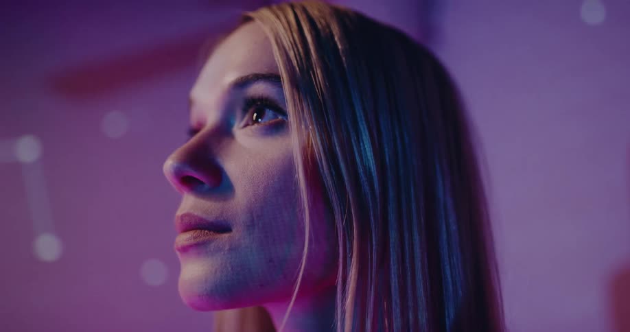 Images of digital circuitry project off a womans face as she stands in front of a wall