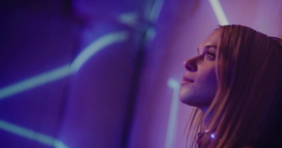 A woman leans her head against a wall as bright lights move on the wall and across the room