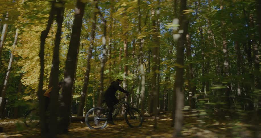 Male and female cyclists cycle through woods and onto path past sign