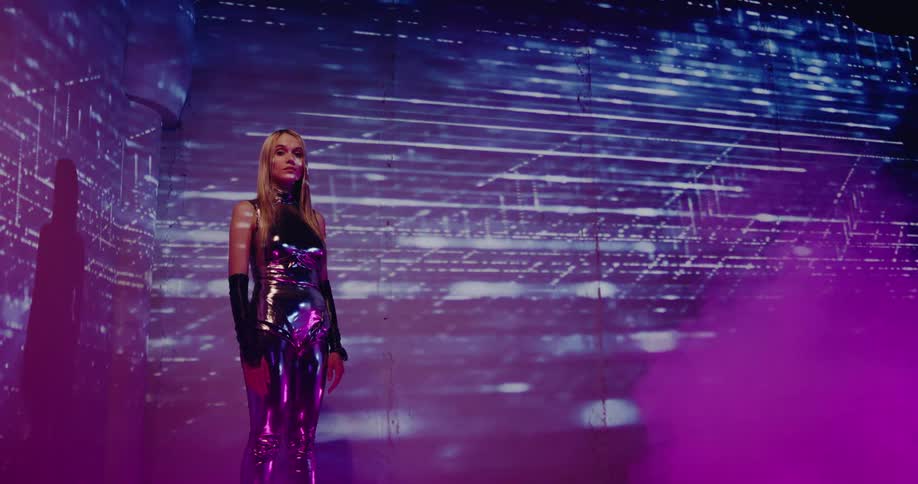 A woman stands in a room with projections of purple light move across the wall