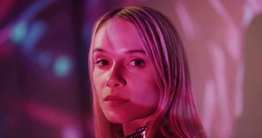 Colored light show flows over blonde womans face and nearby wall