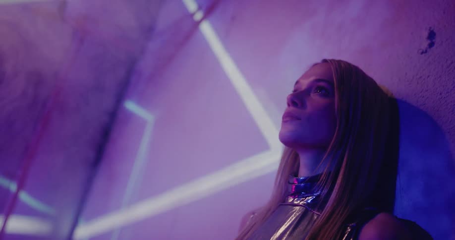 A woman leans against a wall as bright lights flash around her