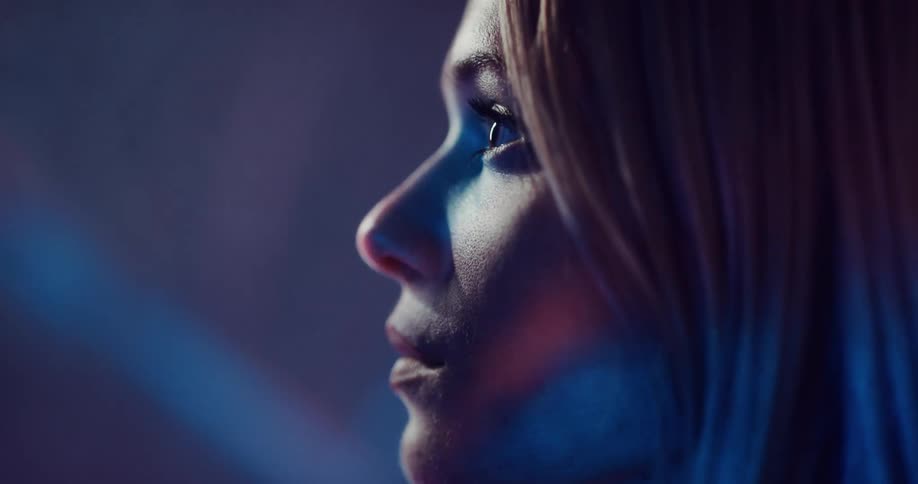 Blonde woman turns her head as colored beams from light show move across her face