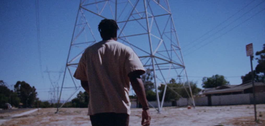 A man slowly walks towards a tall electrical tower on a sunny day