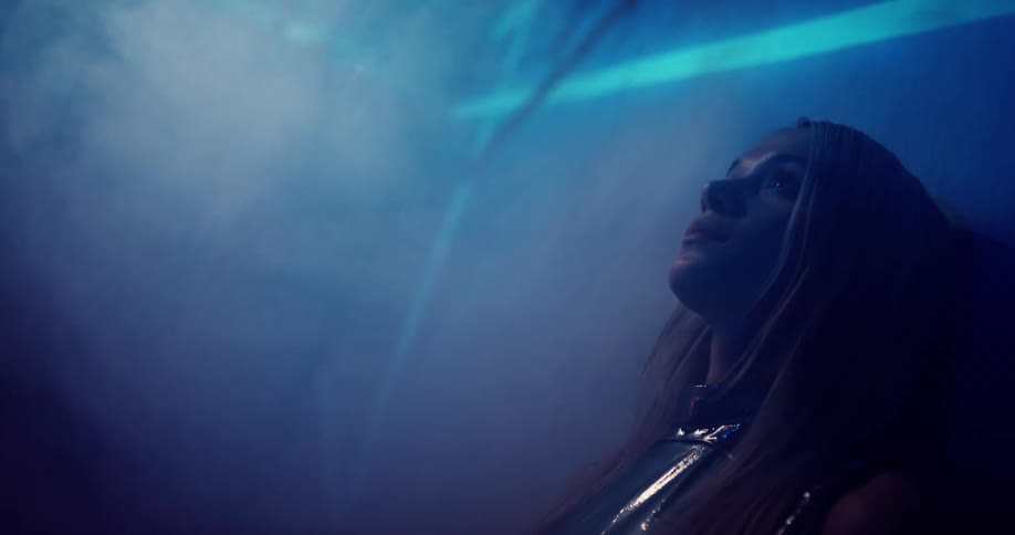 A woman stands with her back against the wall while light is projected around her