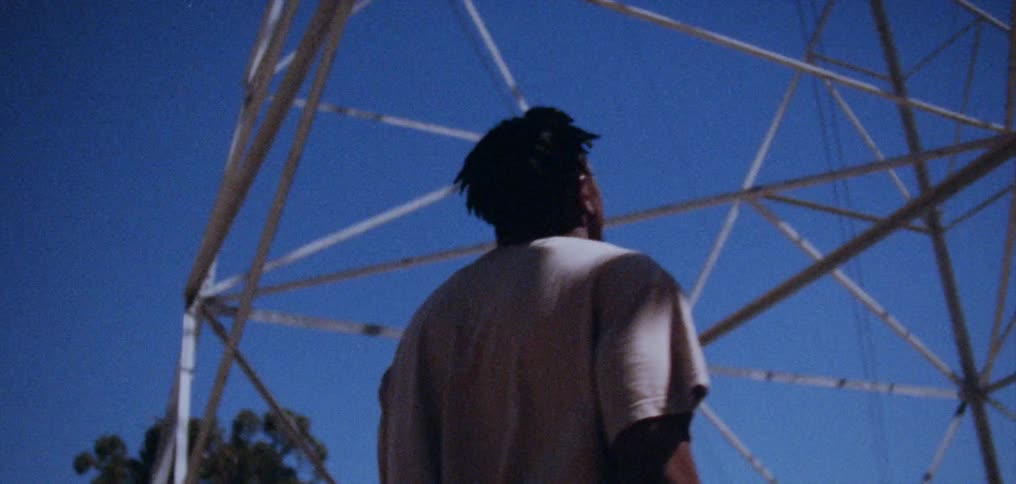 A man is walking under an electrical transmission tower under a clear blue sky