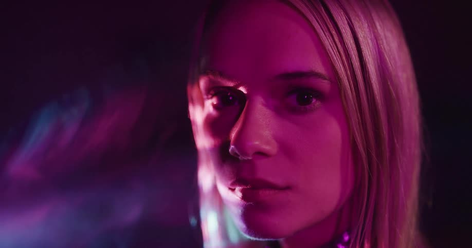 A woman in a room with moving lights and smoke turns her head to the side