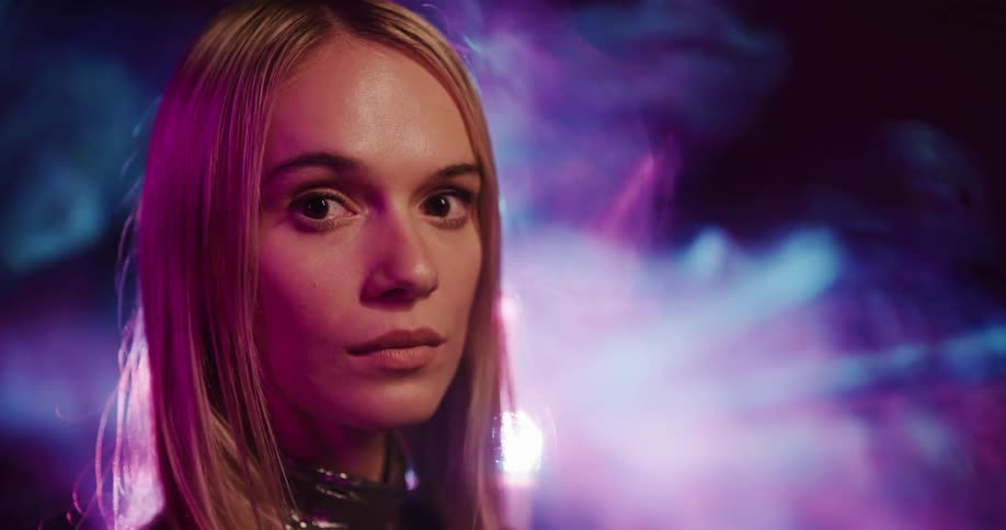 Blonde woman stands backlit by spotlight and colored light show