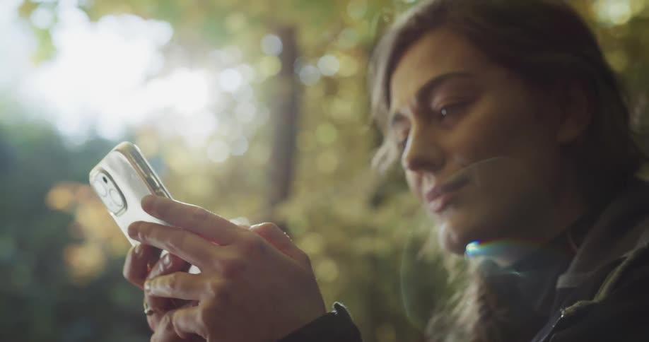 Woman with brown hair uses silver smartphone in the forest
