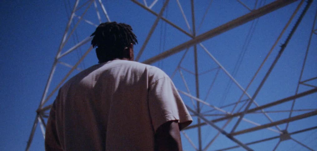 A man is walking under an electrical transmission tower under a clear blue sky