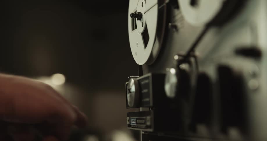 A man switches a button on an old film projector as the film rolls