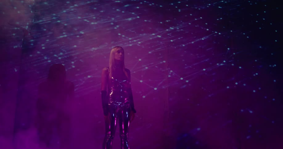 Attractive blonde woman wearing a silver suit stands on a room with smoke and projected lights