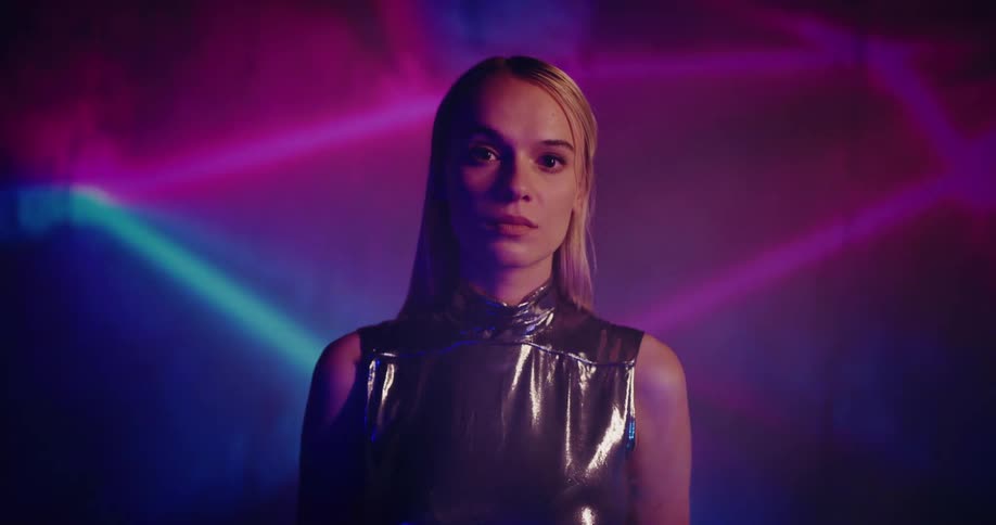 A woman wearing a metallic dress poses in front of a wall of flashing neon lines
